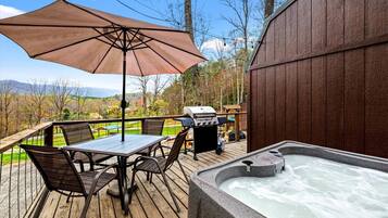 Una terraza de madera con un jacuzzi, una mesa con sillas y una parrilla.