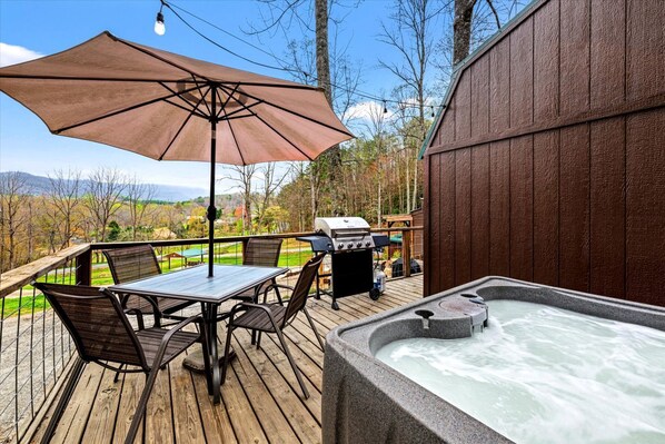 A wooden deck with a hot tub, a table with chairs, and a barbecue grill.