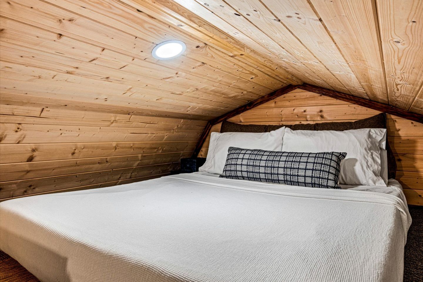 Un dormitorio acogedor en el ático, con techo inclinado, una cama individual con ropa de cama blanca y una mesita de noche pequeña.