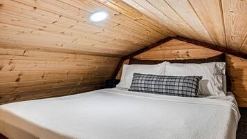 A cozy attic bedroom with a sloped ceiling, a single bed with white bedding, and a small bedside table.