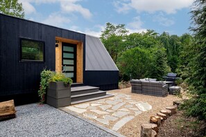 A modern black building with a wooden door, steps leading to a stone pathway, and outdoor furniture.