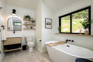 Un bagno moderno con una vasca da bagno freestanding, un water, un lavabo e una finestra con vista su del verde.