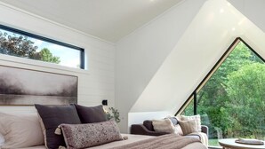 Quarto moderno com uma cama grande, vista para o verde através de um claraboia, e uma mesa redonda com uma cadeira.