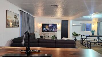 Un salon moderne avec un canapé foncé, une table basse en bois, un téléviseur à écran plat et un coin repas comprenant une table et des chaises.