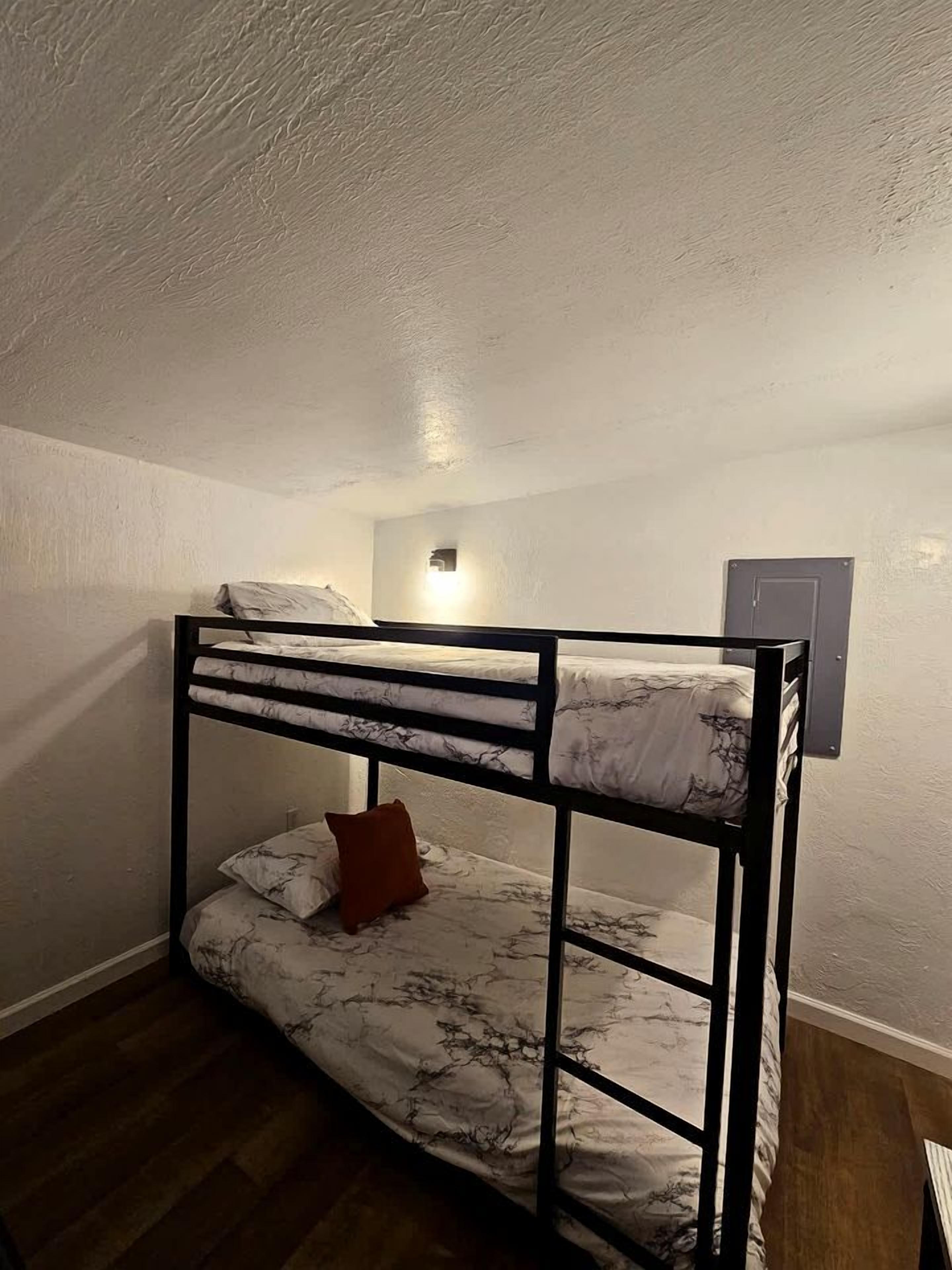 Une chambre avec un lit superposé, un luminaire au-dessus du lit du haut et une porte sur le côté droit.