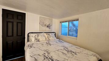 A bedroom with a bed, a window, a door, and a painting on the wall.