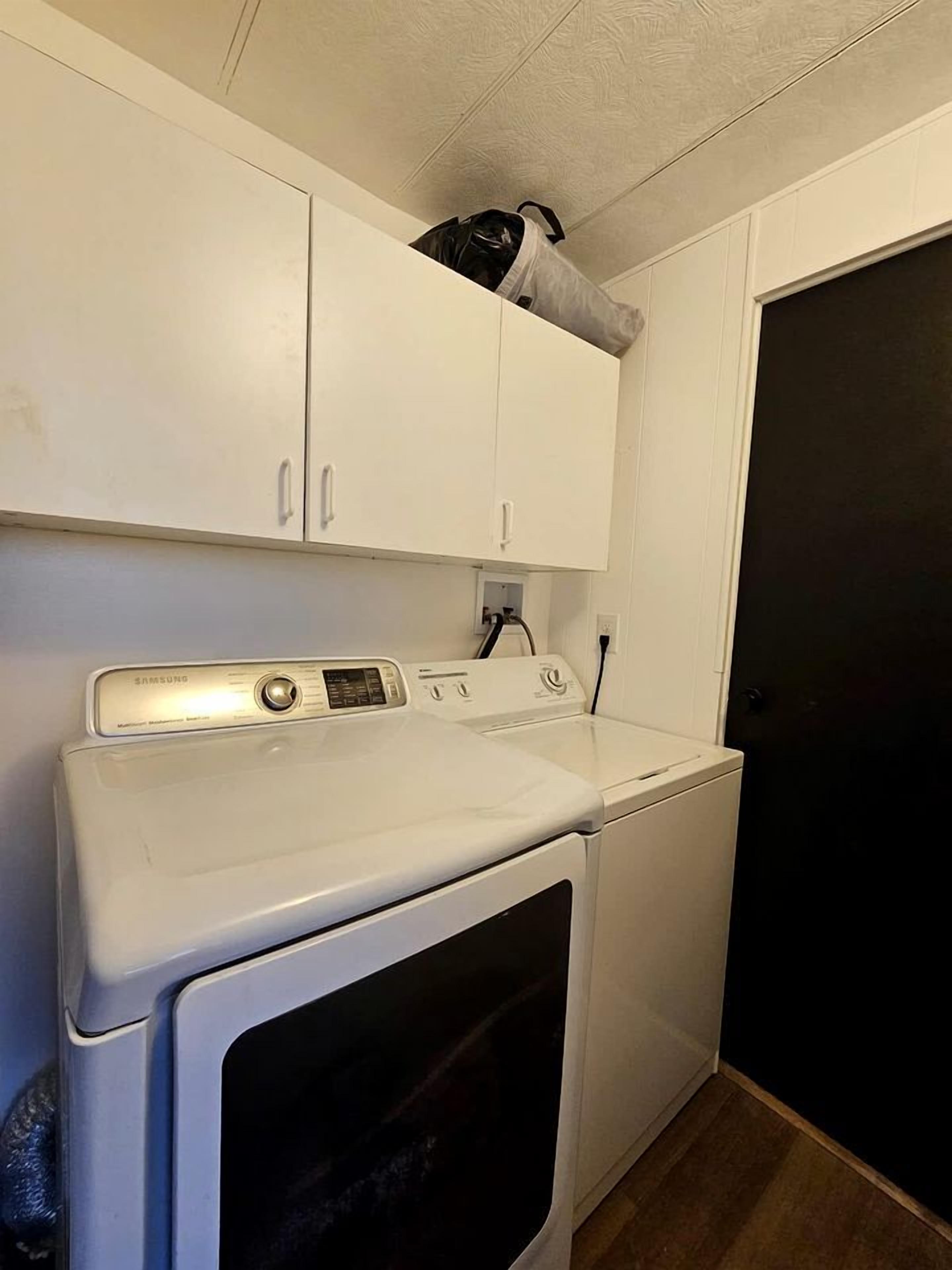 A laundry room with a white washer and dryer, a cabinet above the dryer, and a door to the right.
