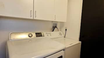 A laundry room with a white washer and dryer, a cabinet above the dryer, and a door to the right.