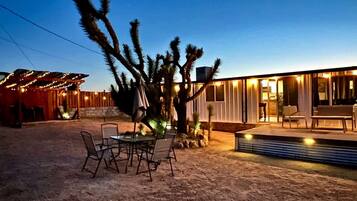 Ein Outdoor-Bereich im Wüstendesign mit Esstisch und Stühlen, einem Kaktus und einem modernen Gebäude mit großen Fenstern.