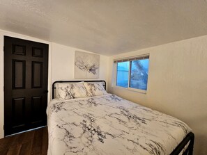 Une chambre à coucher avec un lit, une fenêtre, une porte et une œuvre d’art accrochée au mur.