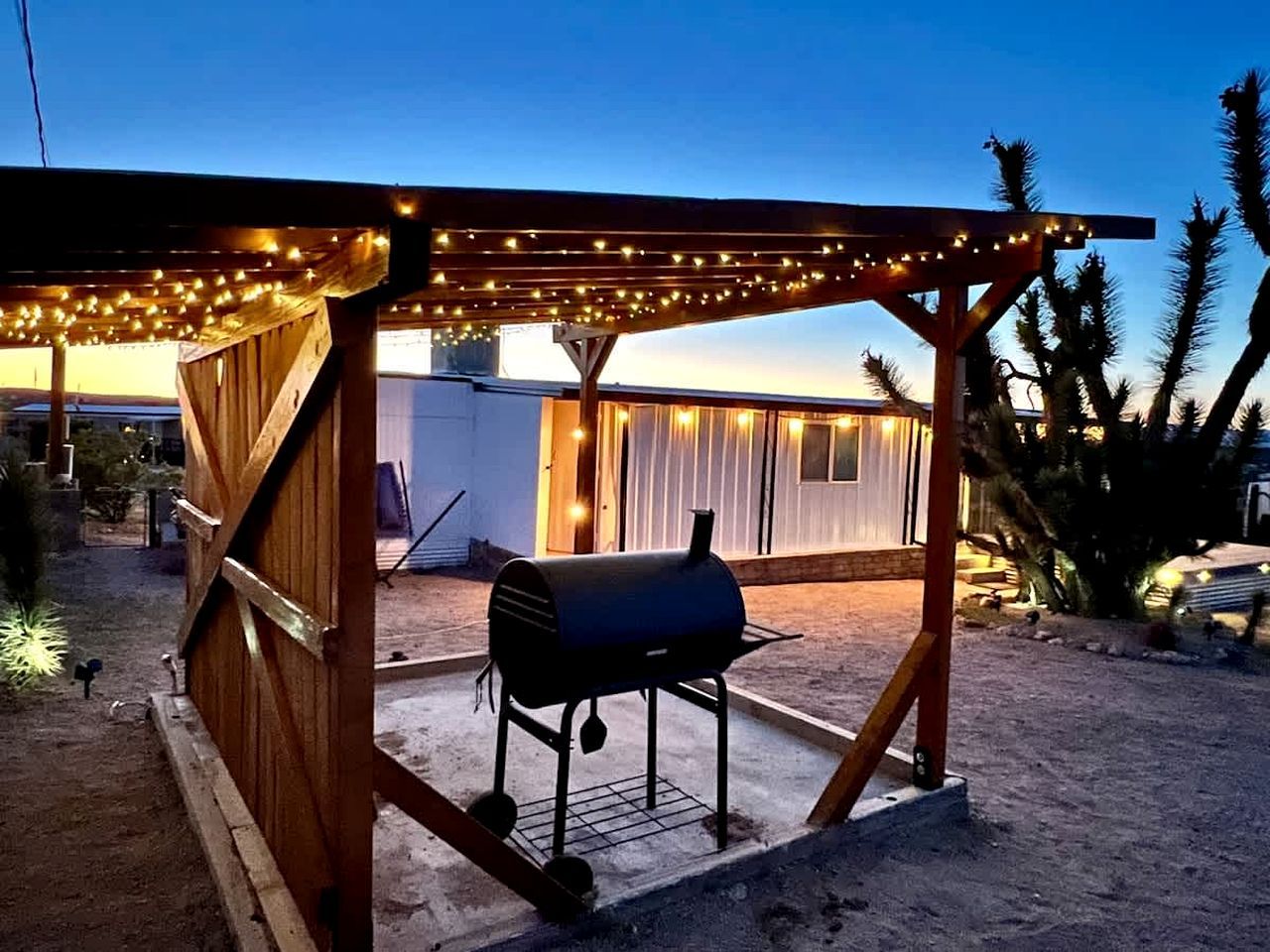 Un espace extérieur abrité comprenant un barbecue, une pergola en bois et des guirlandes lumineuses.