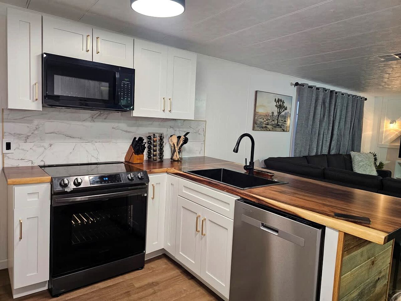 Une cuisine moderne avec des meubles blancs, un micro-ondes noir, une cuisinière et un lave-vaisselle.