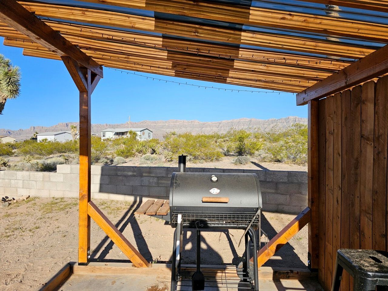 A barbecue grill under a wooden pergola with a clear view of a desert landscape.