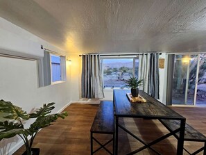 Una habitación con piso de madera, una mesa de madera oscura con un banco, una planta en maceta y vistas al exterior a través de puertas de vidrio grandes.