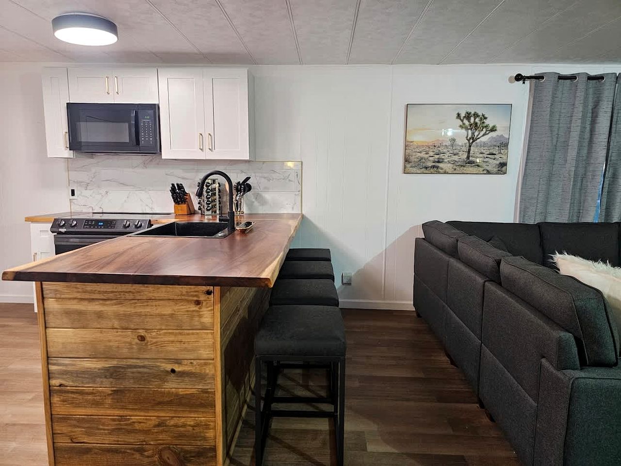 Une cuisine compacte avec des meubles blancs, un îlot central en bois et un micro-ondes noir.