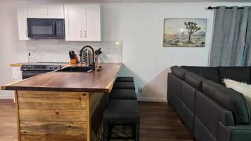 Une cuisine compacte avec des meubles blancs, un îlot central en bois et un micro-ondes noir.