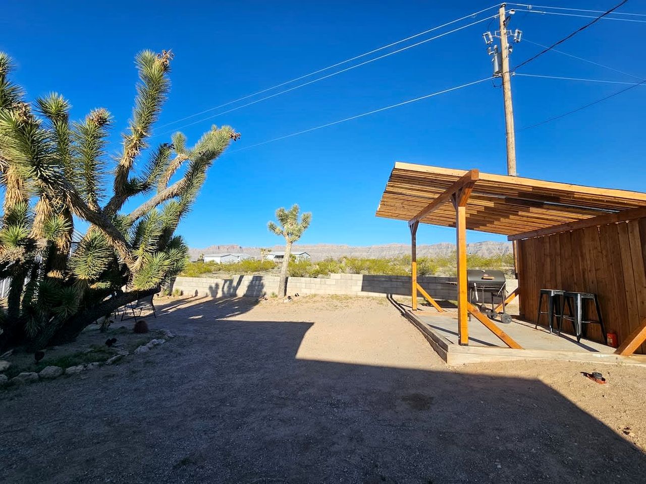 Un paysage désertique avec une structure en bois, un grand cactus et des montagnes à l’horizon.