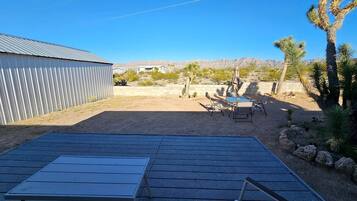 Un espace patio avec une table et des chaises en métal, une piscine et, en arrière-plan, un paysage désertique.
