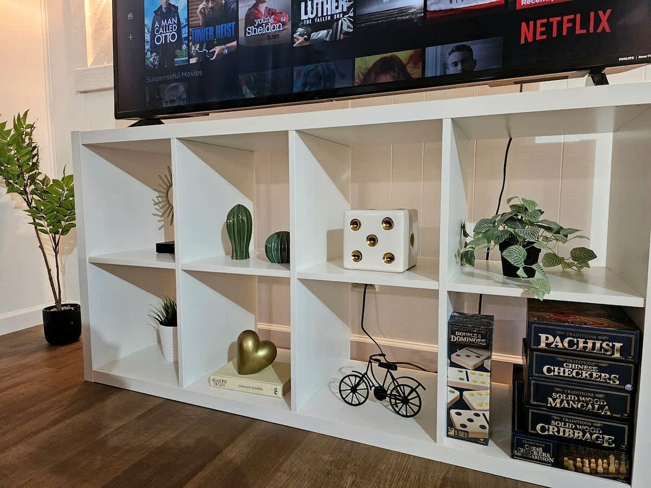 Une étagère blanche ornée d’objets décoratifs, un téléviseur diffusant du contenu Netflix et une plante.
