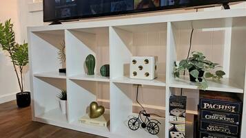 Une étagère blanche ornée d’objets décoratifs, un téléviseur diffusant du contenu Netflix et une plante.