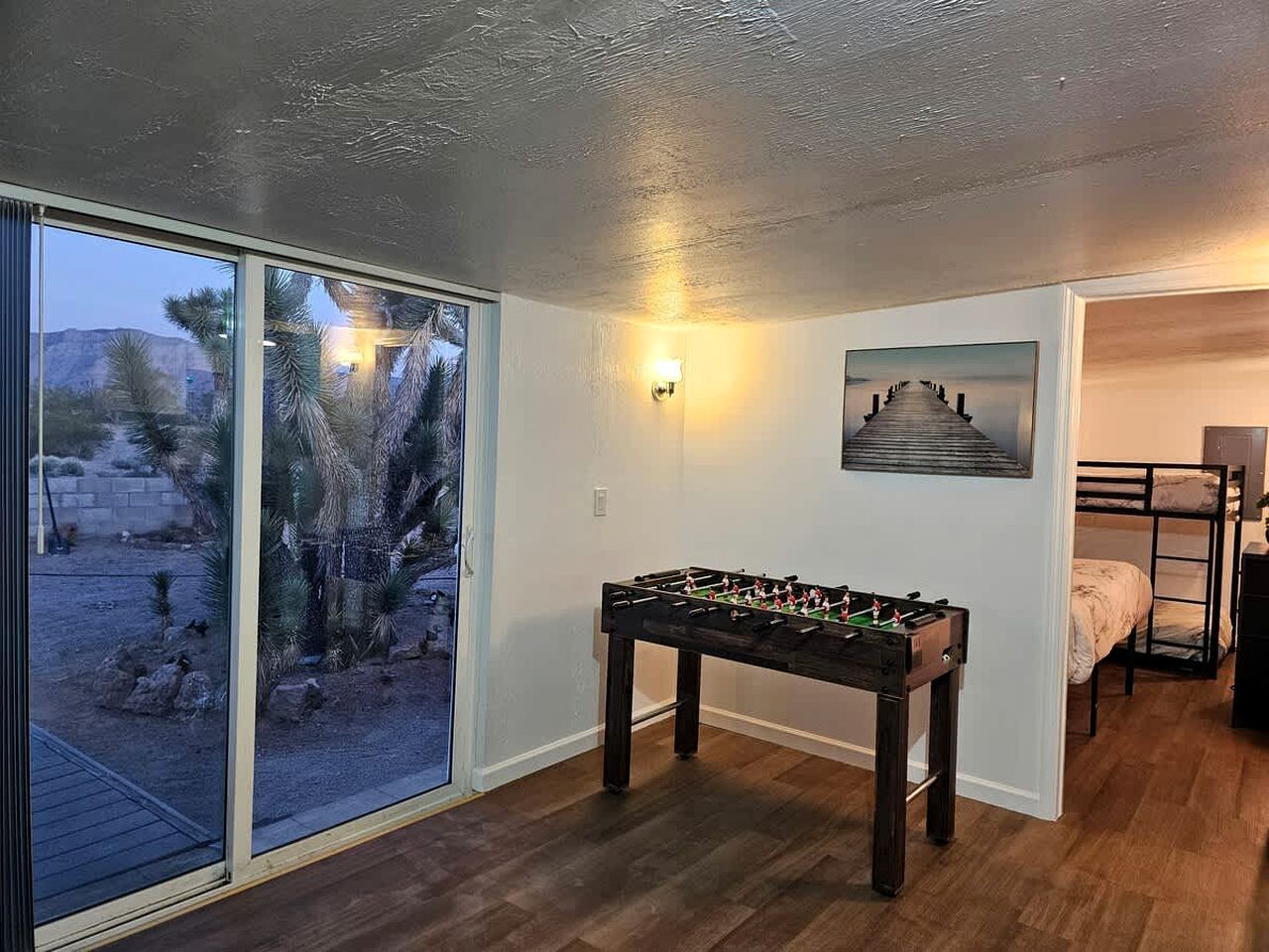 Une pièce avec une table de baby-foot, un lit superposé et une grande fenêtre donnant sur un paysage désertique.