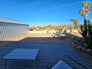 A patio with a table and chairs, a building, and desert vegetation.