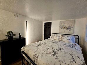 Une chambre à coucher avec un lit, une commode, une plante en pot et un tableau accroché au mur.