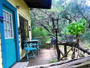 A wooden deck with a table and chairs, a blue door, and a hanging plant.