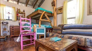 A rustic room with a bunk bed, a wooden table, a striped sofa, and a pink chair.