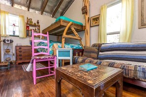 A rustic room with a bunk bed, a wooden table, a striped sofa, and a pink chair.