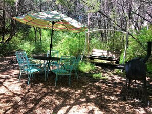 Un coin pique-nique aménagé avec une table, des chaises et un barbecue dans un espace boisé.