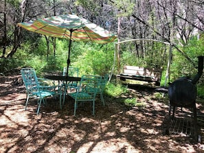 A picnic setup with a table, chairs, and a grill in a wooded area.