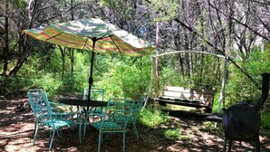 A picnic setup with a table, chairs, and a grill in a wooded area.
