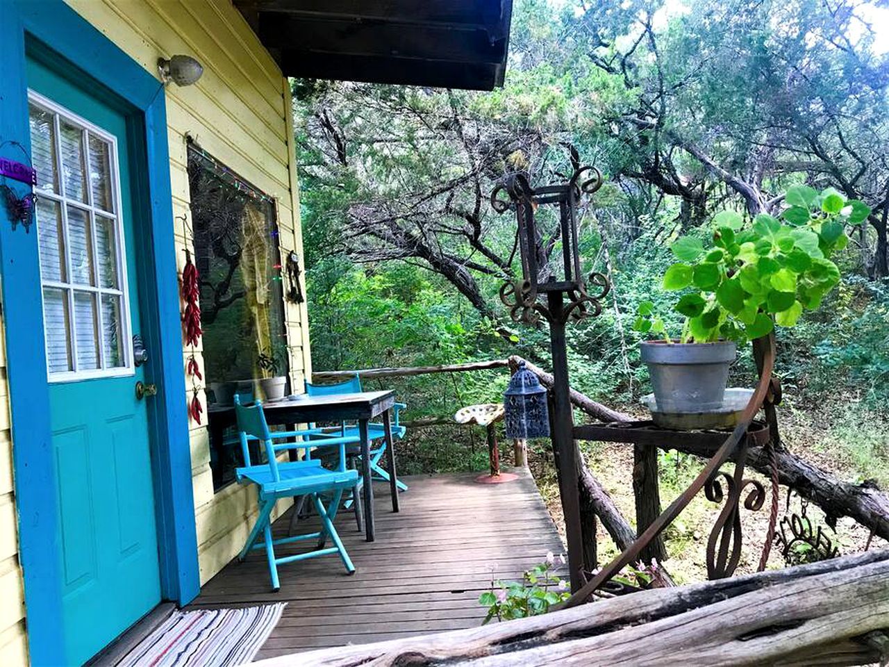 A wooden deck with a table and chairs, a blue door, and a hanging plant.