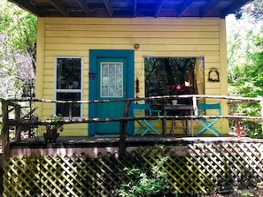 A yellow building with a blue door and windows, a wooden deck with chairs, and a lattice fence.