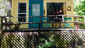 A yellow building with a blue door and windows, a wooden deck with chairs, and a lattice fence.