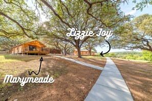 Une cabane en bois dotée d’un porche, entourée d’arbres et accessible par un sentier bien dégagé.
