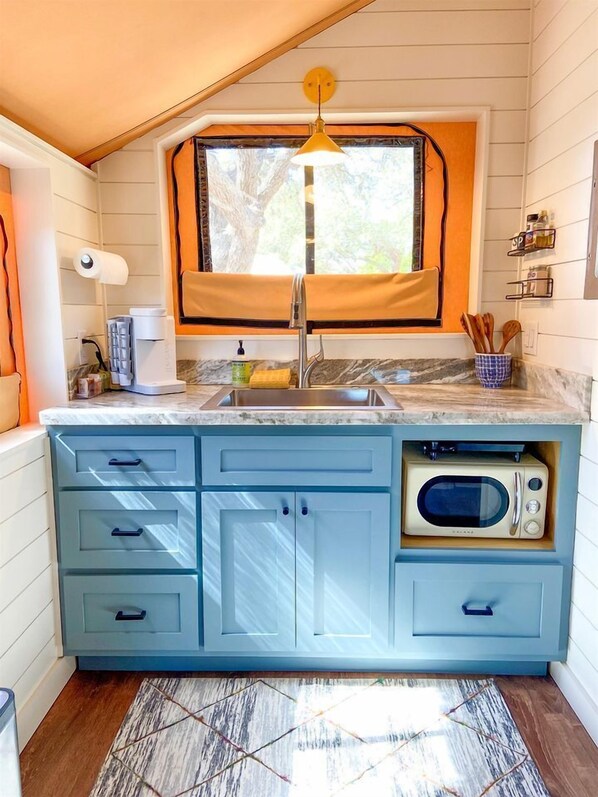 A kitchen with a built-in microwave, a sink, and a window with a curtain.