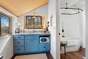 Een kleine keuken met een inbouwoven, een raam boven de spoelbak, en een douche met gordijn.