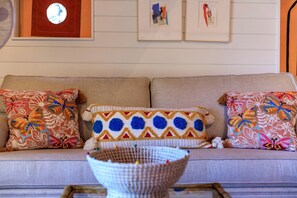 A sofa with patterned cushions, a wall clock, and framed pictures.