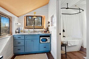 A compact kitchen with a built-in oven, a window above the sink, and a shower area with a curtain.