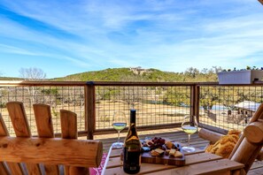 A wooden deck with a table set for a meal, a bottle of wine, and two glasses.