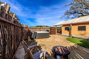 Un jardin avec un jacuzzi, un foyer extérieur, une clôture en bois et un bâtiment doté d’un patio couvert.