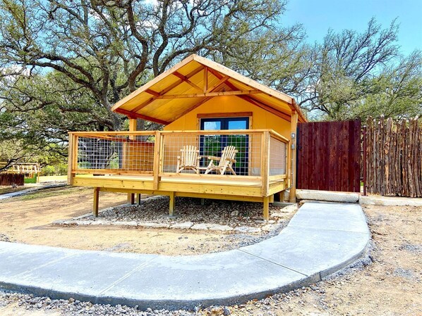 A wooden cabin with a fenced porch, two chairs, and a window.