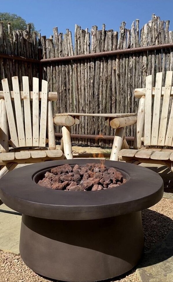 A circular fire pit with logs, surrounded by wooden Adirondack chairs.