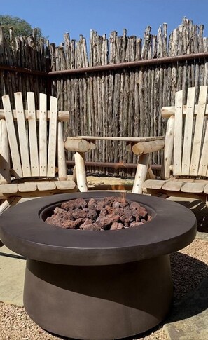 Un pozo de fuego circular con leña, rodeado de sillas Adirondack de madera.