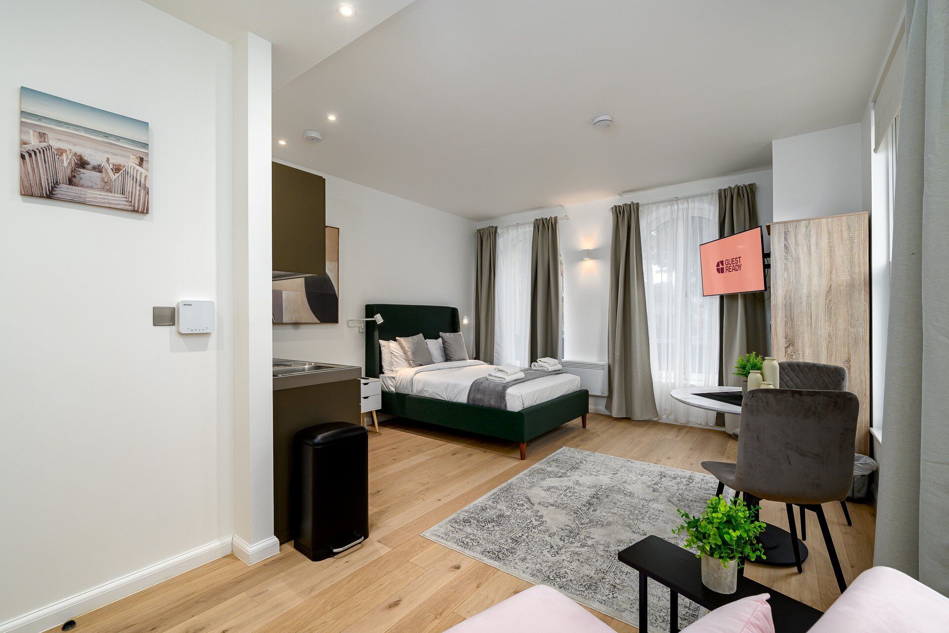 A modern hotel room with a bed, a desk, a chair, a TV, and a small plant.