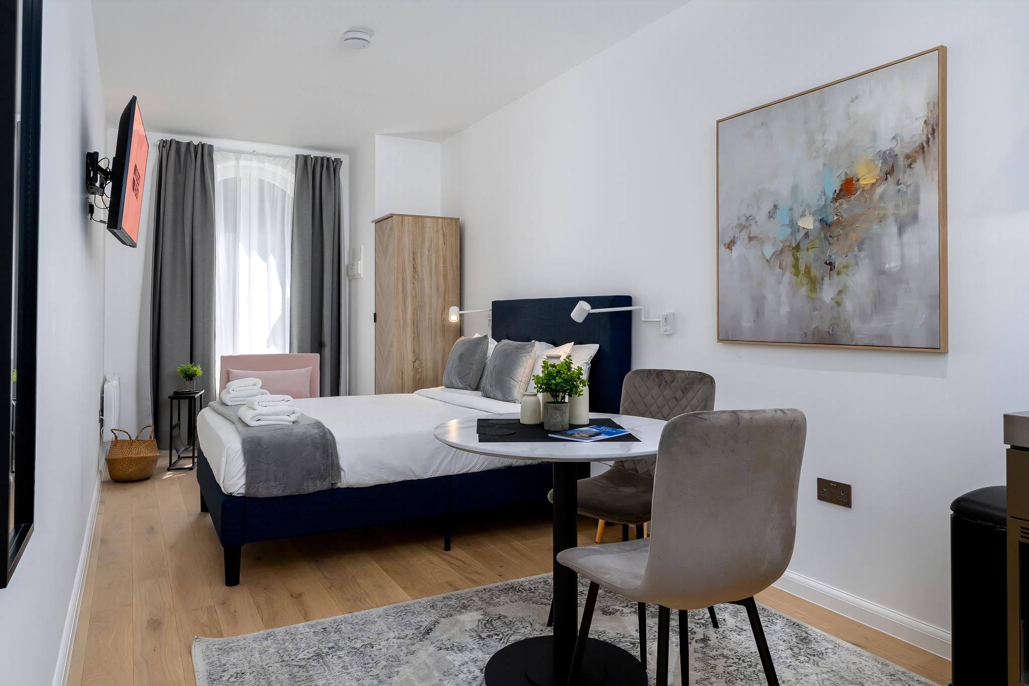 A modern bedroom with a bed, bedside table, chair, and a large abstract painting.