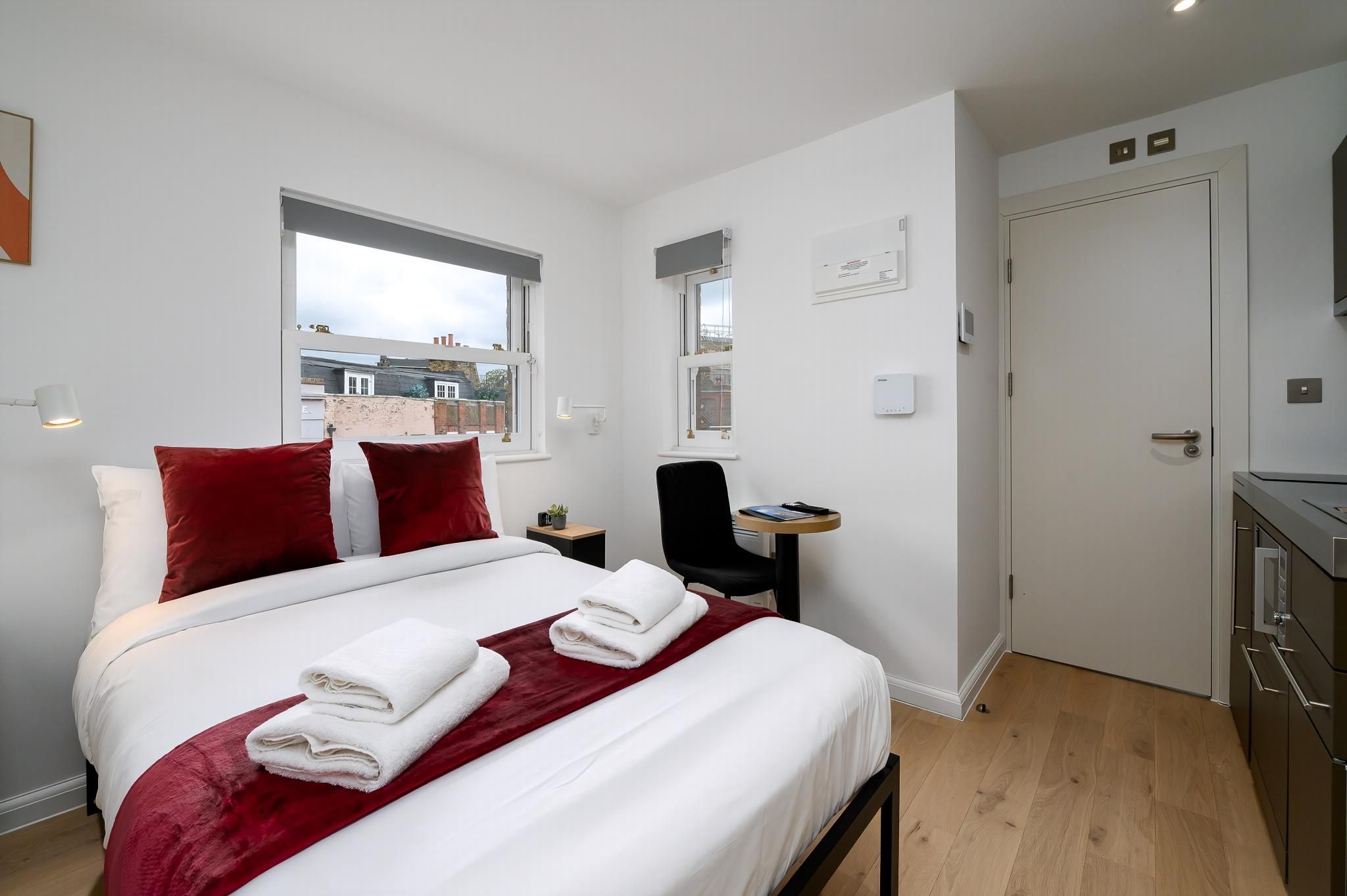 A hotel room with a bed, a desk, a chair, a door, and a window.