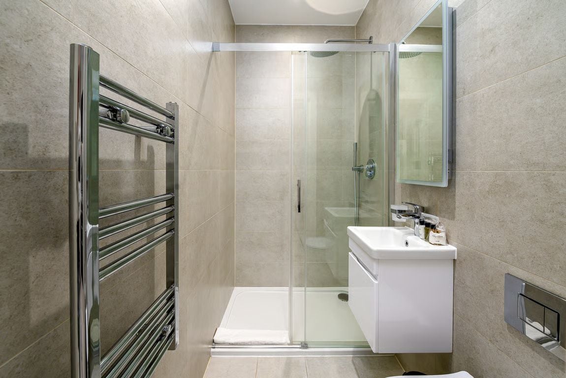 A modern bathroom with a glass shower enclosure, a white sink, and a chrome towel rack.
